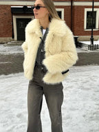 Woman in a cream faux fur jacket over a grey t-shirt and grey wide-leg jeans, accessorized with sunglasses and a necklace.