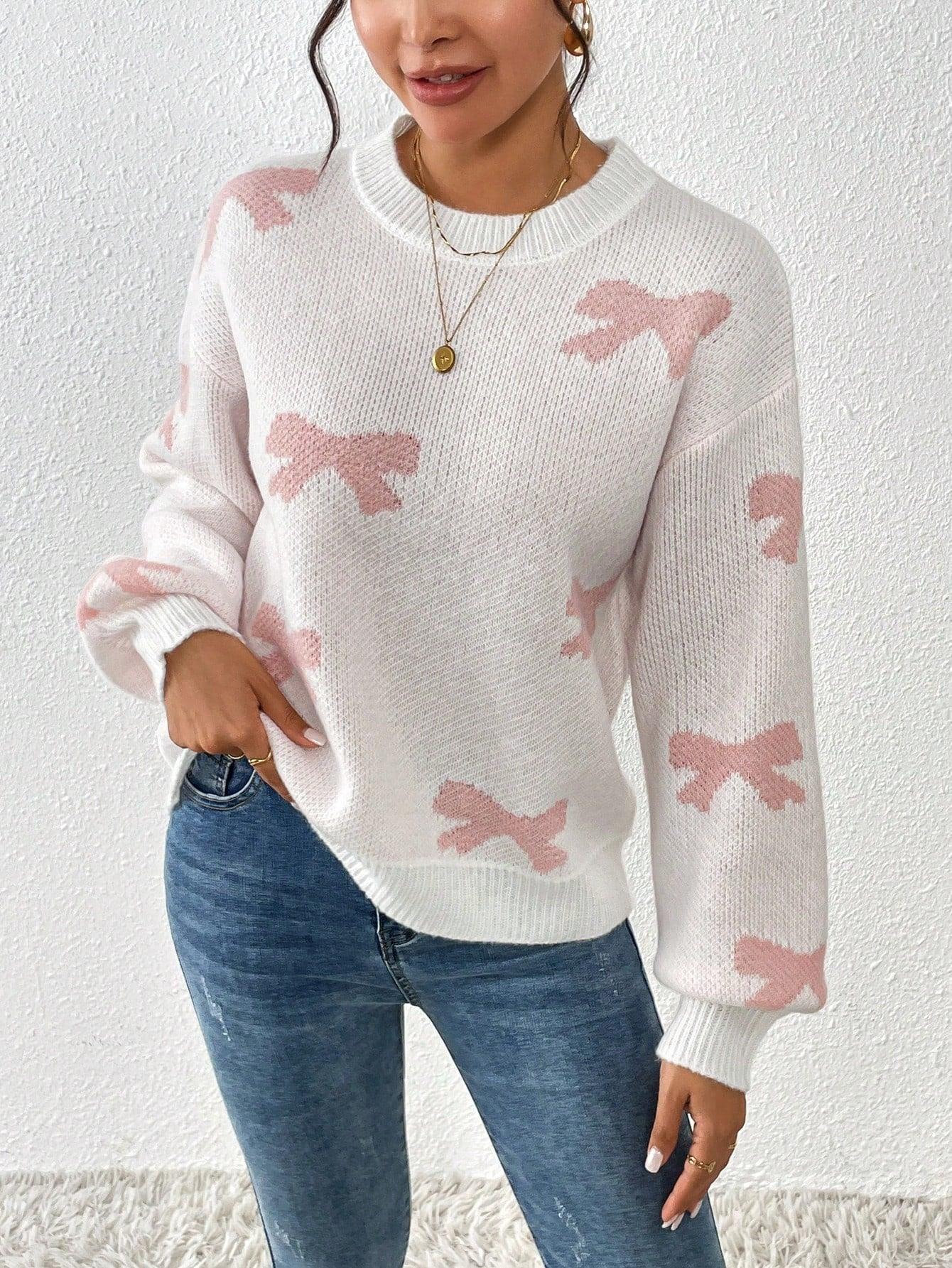Front view of a woman in a white knit sweater with a pink bow print and crew neckline, holding her hand on her hip.