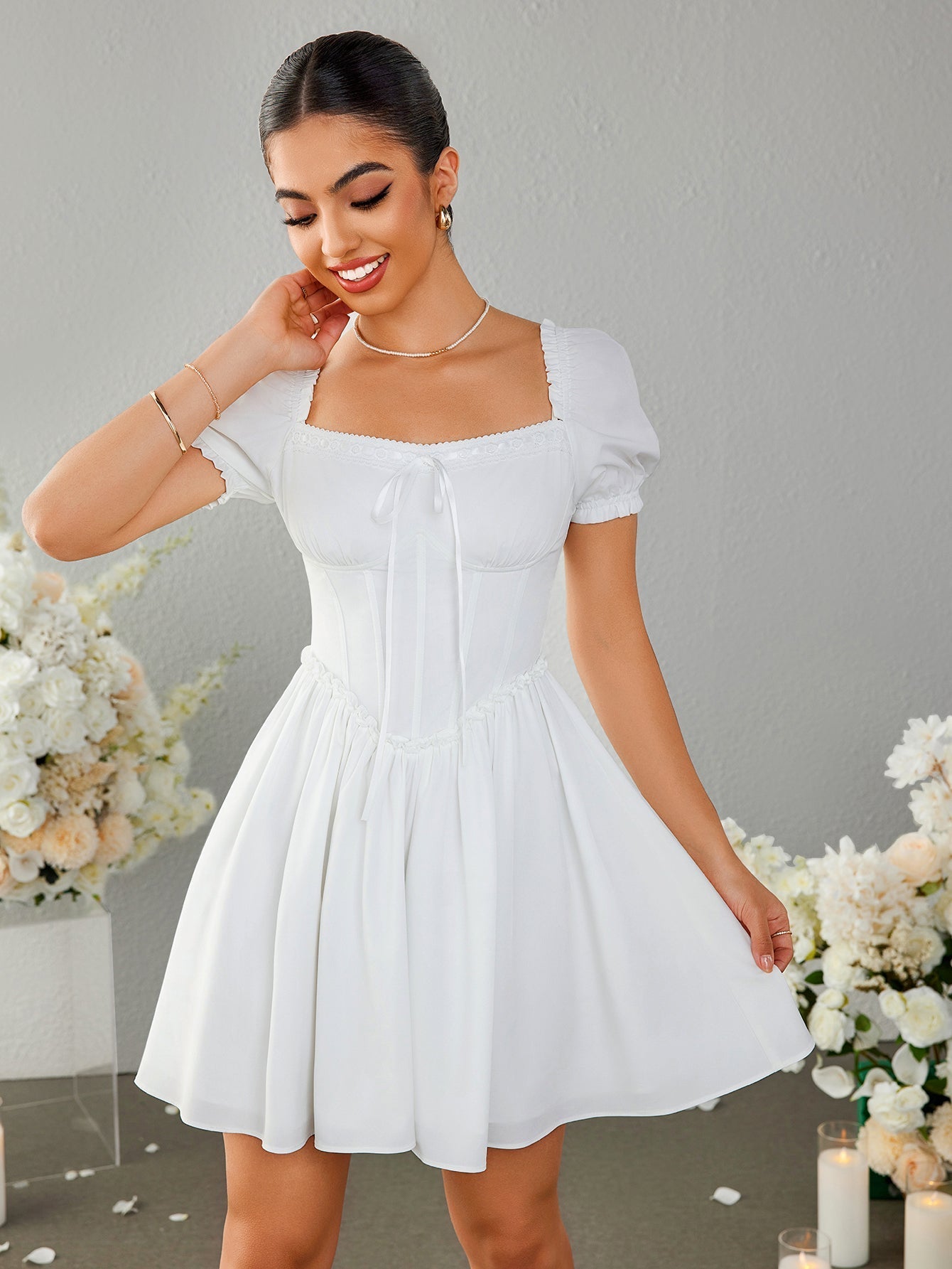 Woman smiling and adjusting her white off-the-shoulder dress with puff sleeves.