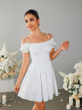 Woman posing in a white off-the-shoulder dress with lace trim and a tie detail.