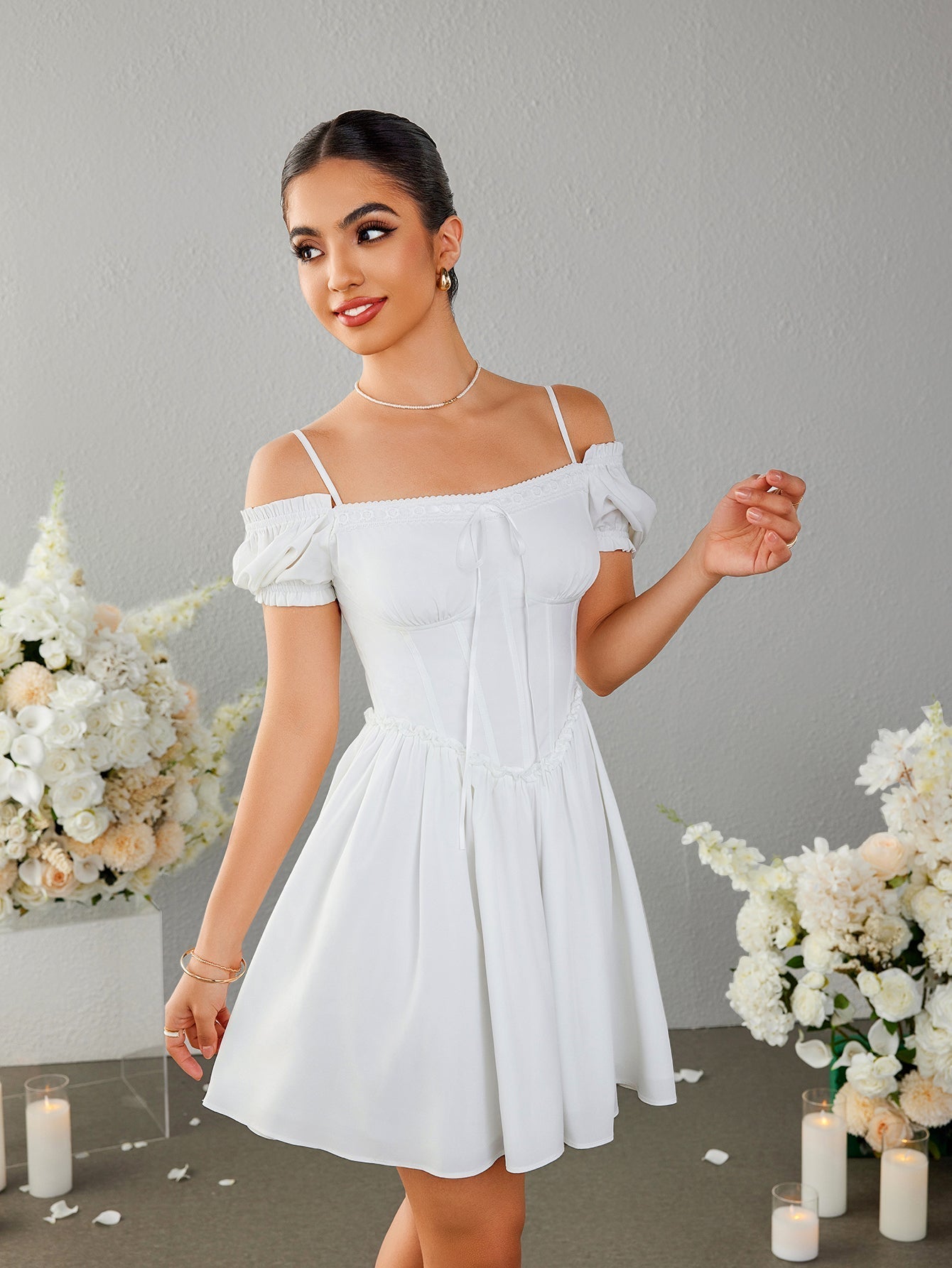 Woman posing in a white off-the-shoulder dress with lace trim and a tie detail.