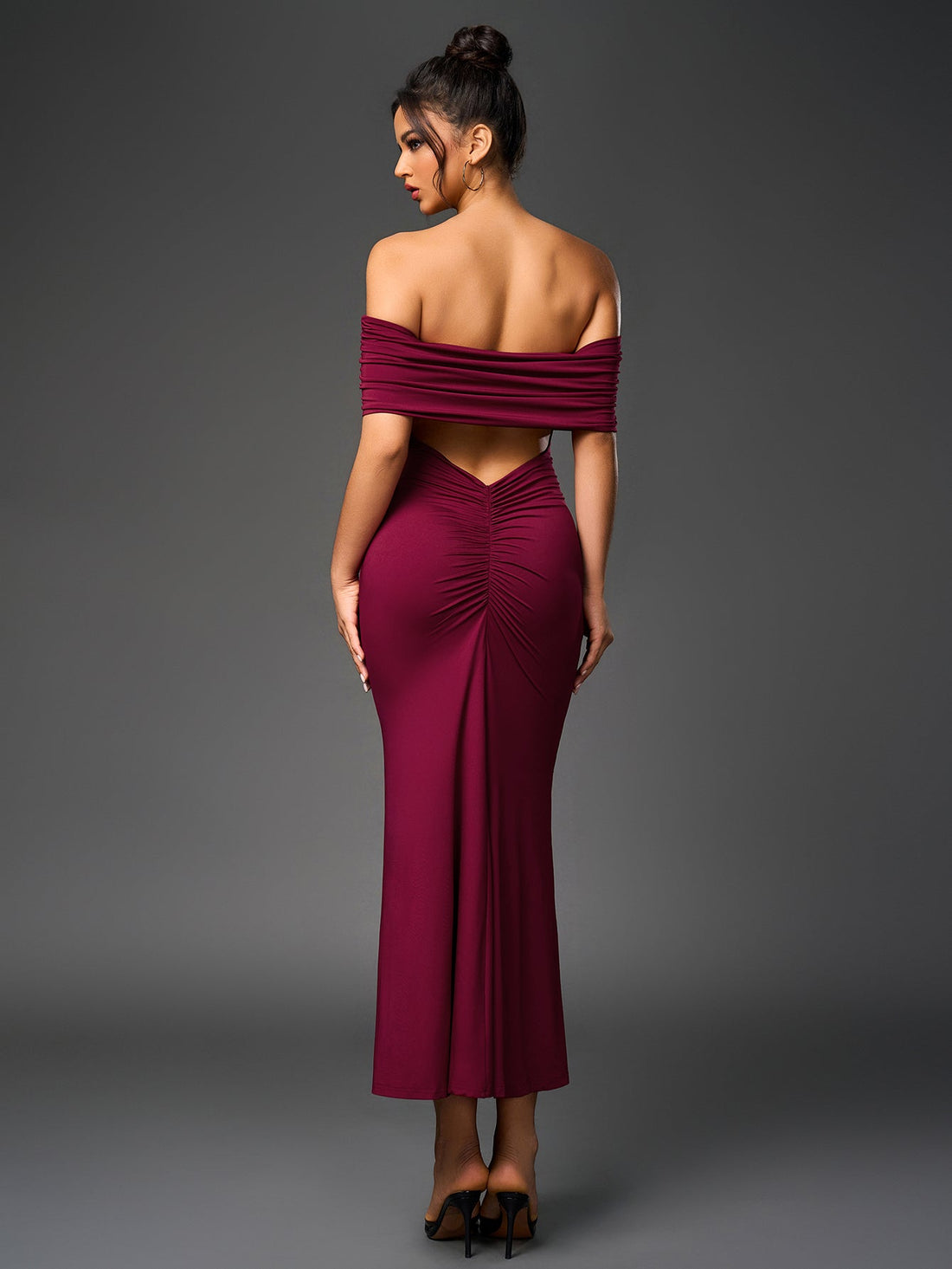 Woman wearing a floor-length, off-the-shoulder maroon dress with ruched detailing on the back.