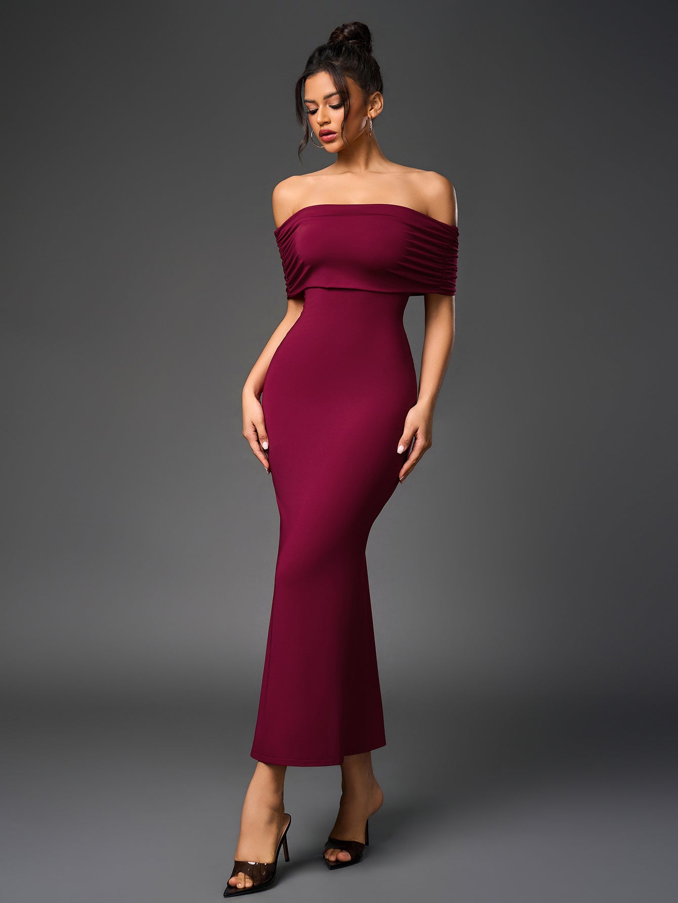 Front view of a woman modeling a fitted, off-the-shoulder maroon gown with a mermaid silhouette.