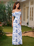 Woman wearing a white maxi dress with a blue floral print and off-the-shoulder neckline posing in a garden.