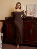 Woman leaning on a wooden cabinet wearing a long brown off-the-shoulder gown