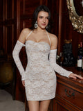Woman in a white lace mini dress with off-the-shoulder long sleeves and a halter neckline, standing by a wooden dresser.