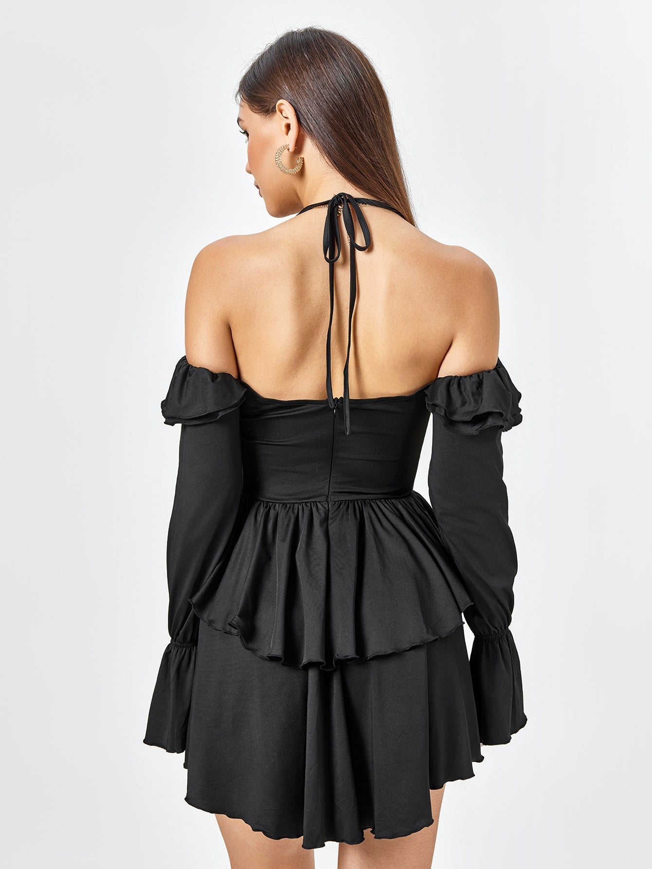 Back view of a woman in a black tiered dress with long sleeves.