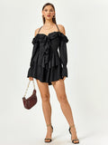 Full body shot of a woman in a black halter neck dress with tiered ruffles and long sleeves, holding a handbag.