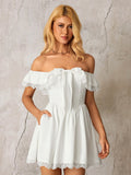 Woman in a white off-the-shoulder dress with ruffled and lace trim, and a bow detail, showing the dress's side pockets.