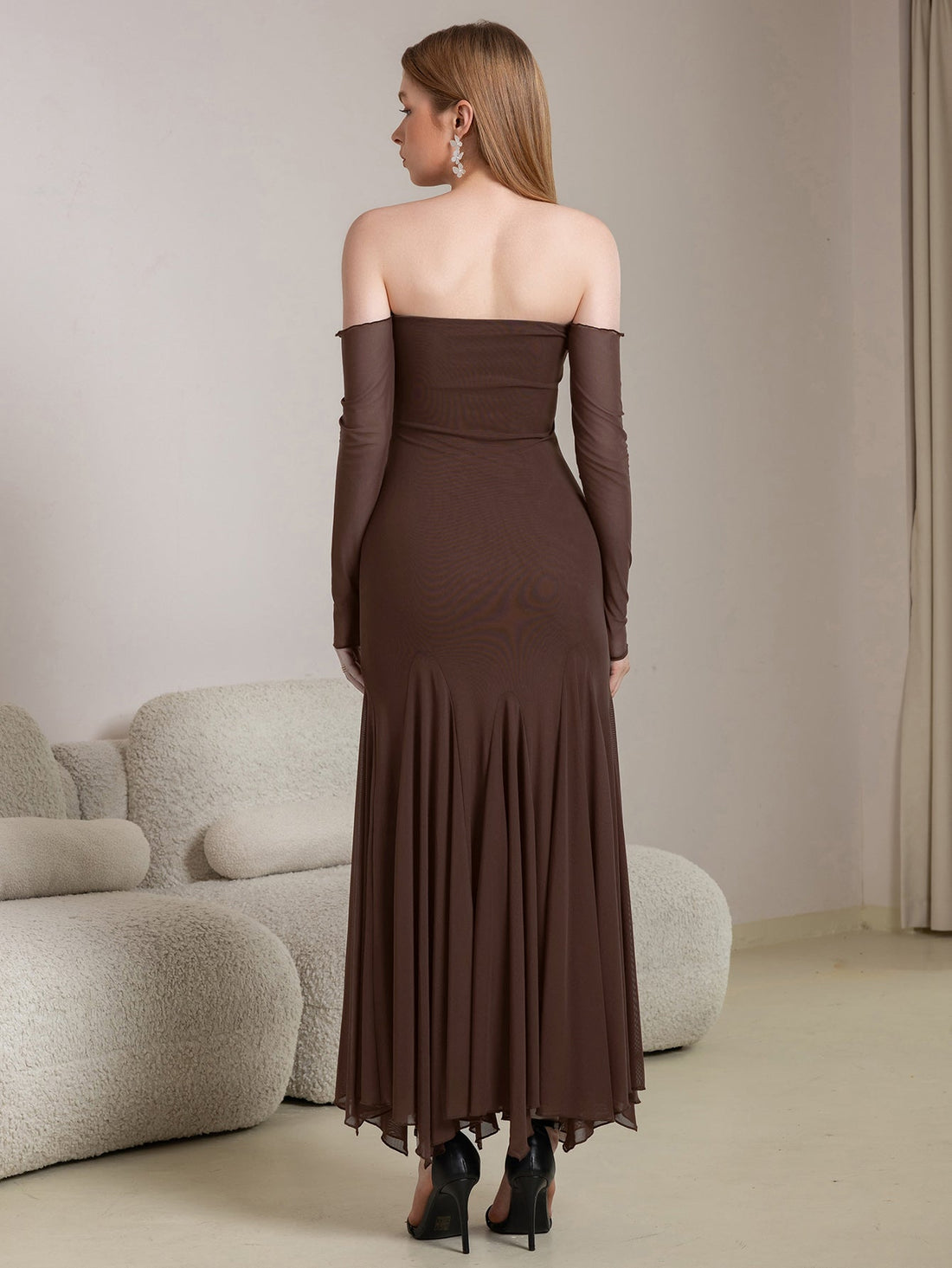 Woman wearing a long brown off-the-shoulder dress with sheer long sleeves and a mermaid hem