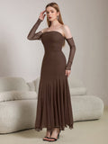 Woman adjusting her hair while wearing a long brown off-the-shoulder dress with sheer sleeves