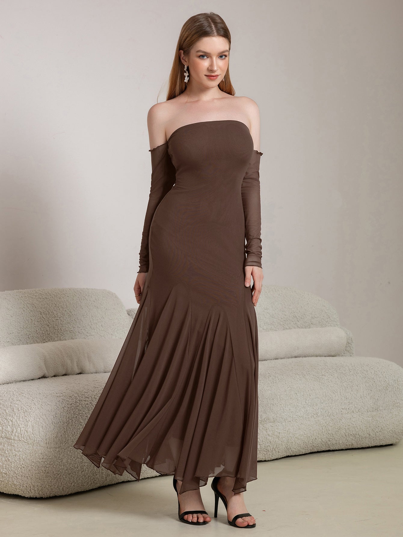Woman posing in a long brown strapless dress with sheer sleeves and a flared hem