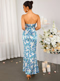 Rear view of a woman in a long, strapless, white dress with a blue floral print and a mermaid silhouette.