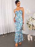 Full-length shot of a woman in a strapless floral print maxi dress with a mermaid silhouette, holding a woven handbag.