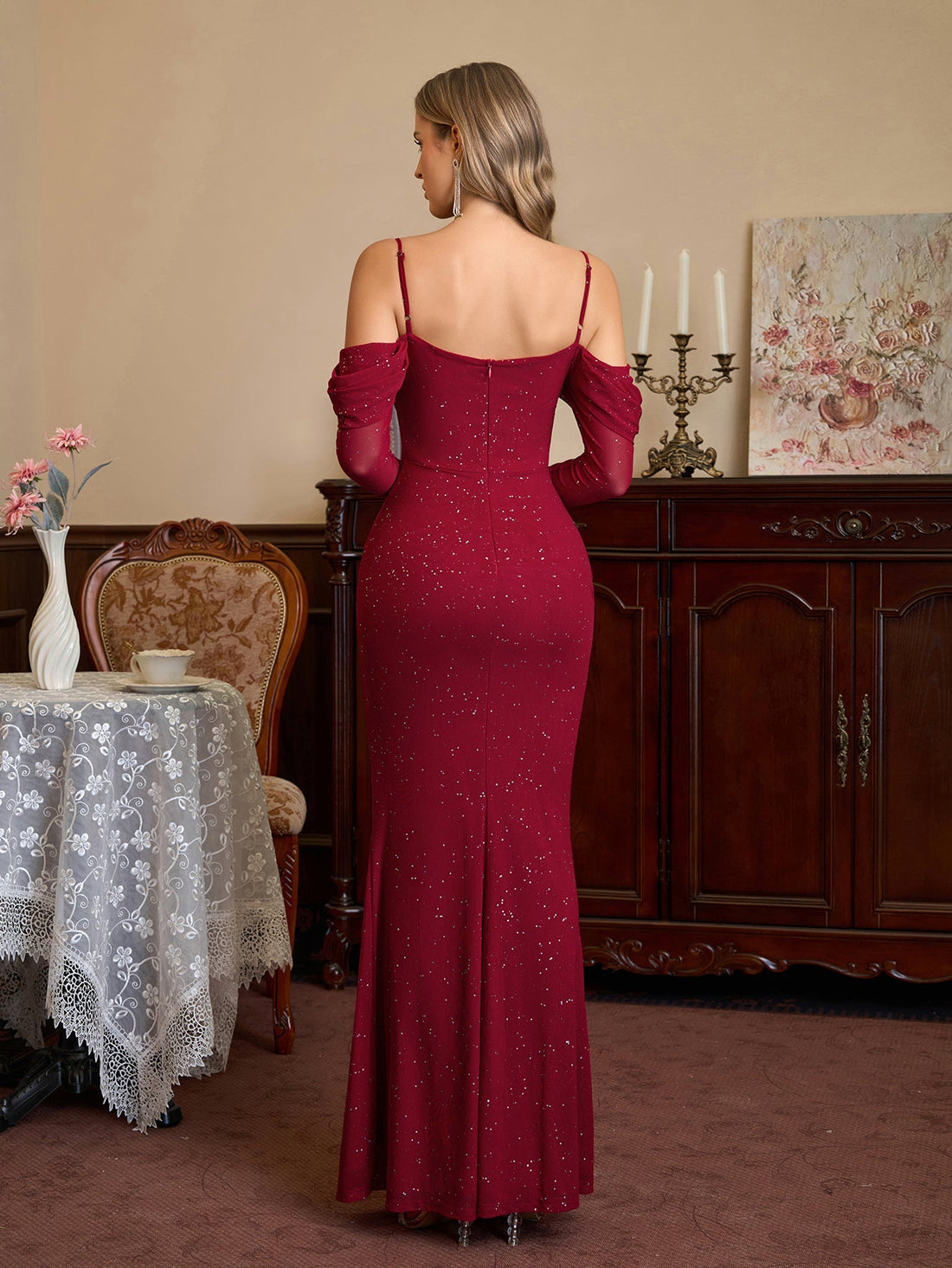 Woman in a red sparkle mermaid gown with off-the-shoulder long sleeves standing.