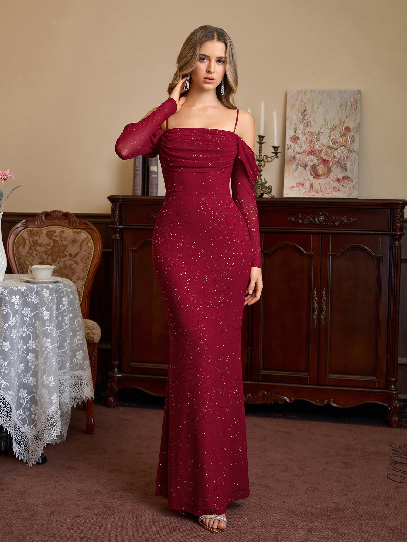 Woman in a red sparkle mermaid gown with off-the-shoulder long sleeves adjusting her hair.
