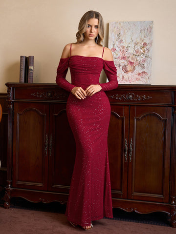 Woman in a red sparkle mermaid gown with off-the-shoulder long sleeves standing.