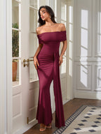 Woman wearing a floor-length burgundy off-the-shoulder dress with ruched detailing and a mermaid hem.