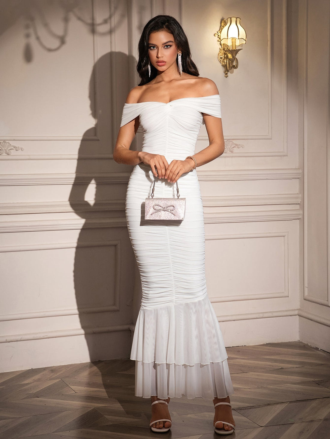 Woman wearing a white off-the-shoulder ruched mermaid gown with a ruffled hem