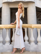 Woman in a white one-shoulder crepe dress with cut-out detail and ruched tie waist, standing on a balcony.