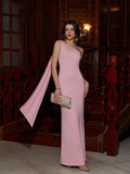 Woman in a pink one-shoulder maxi dress with draped detailing and a clutch bag standing on a wooden staircase.