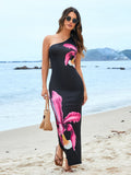 Woman wearing a black one-shoulder maxi dress with a large pink floral print on the beach.