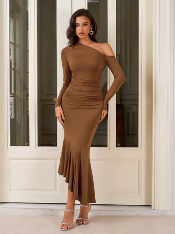 Woman wearing a brown one-shoulder long sleeve dress with ruching and a ruffle hem, standing in front of a white door.