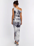Back view of a woman in a grey and white abstract print asymmetrical sleeveless top and matching maxi skirt with a high slit.