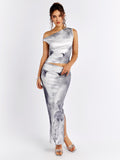 Woman wearing a grey and white abstract print asymmetrical sleeveless top and matching maxi skirt with a high slit.