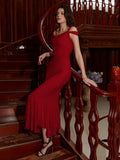 Woman in a red one-shoulder mermaid gown with cold-shoulder detail posing on a wooden staircase.