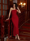 Woman in a red one-shoulder mermaid gown with cold-shoulder detail leaning on a wooden banister.