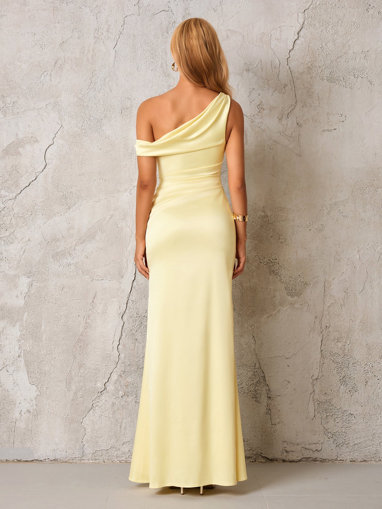 Back view of a woman in a pale yellow satin one-shoulder floor-length column dress
