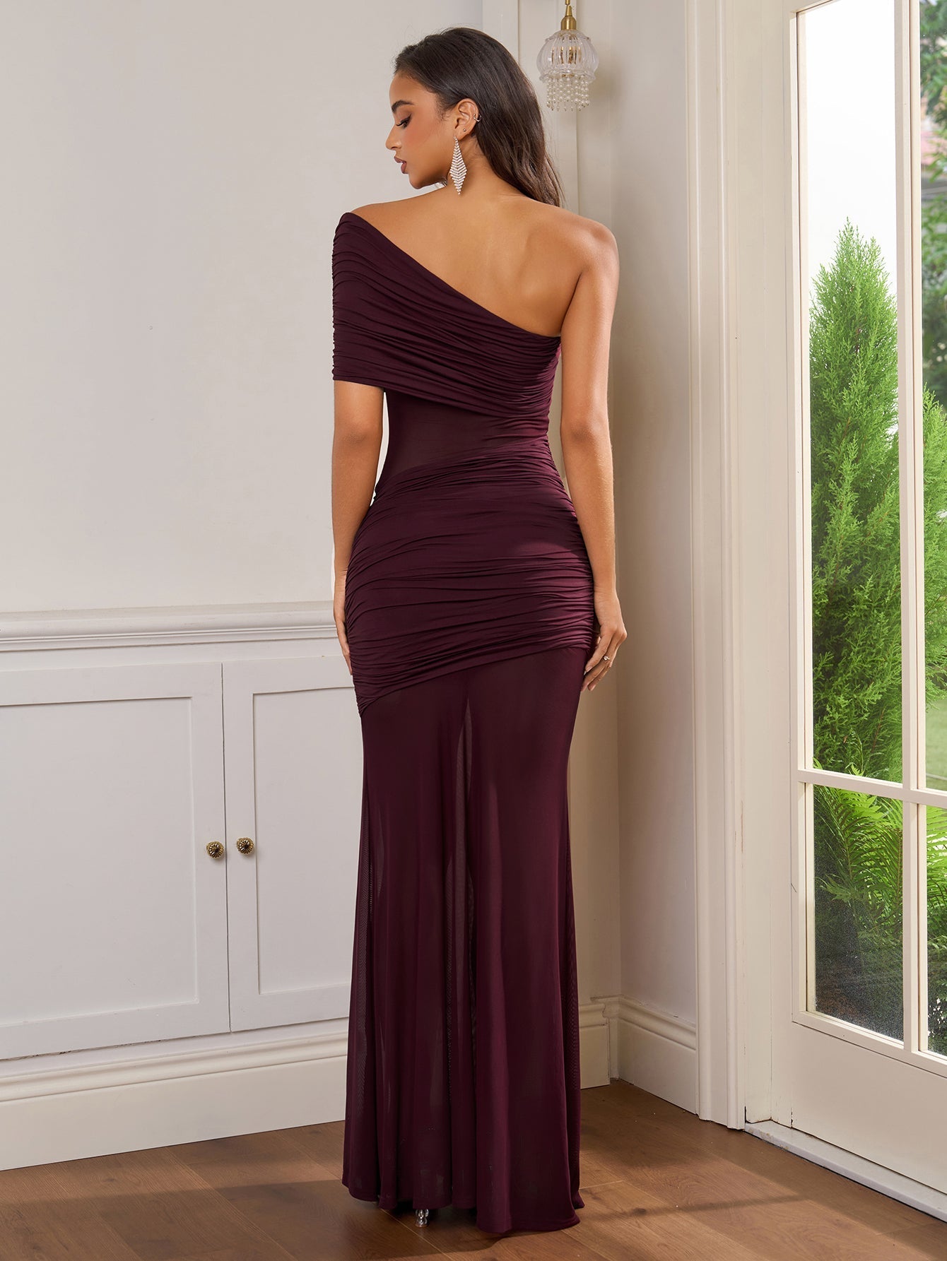Back view of a burgundy one-shoulder ruched gown with sheer panels