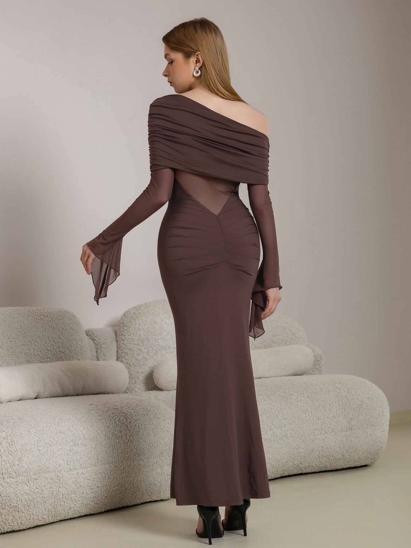 Back view of a woman in a long brown dress with flared sleeves and a V-shaped sheer panel