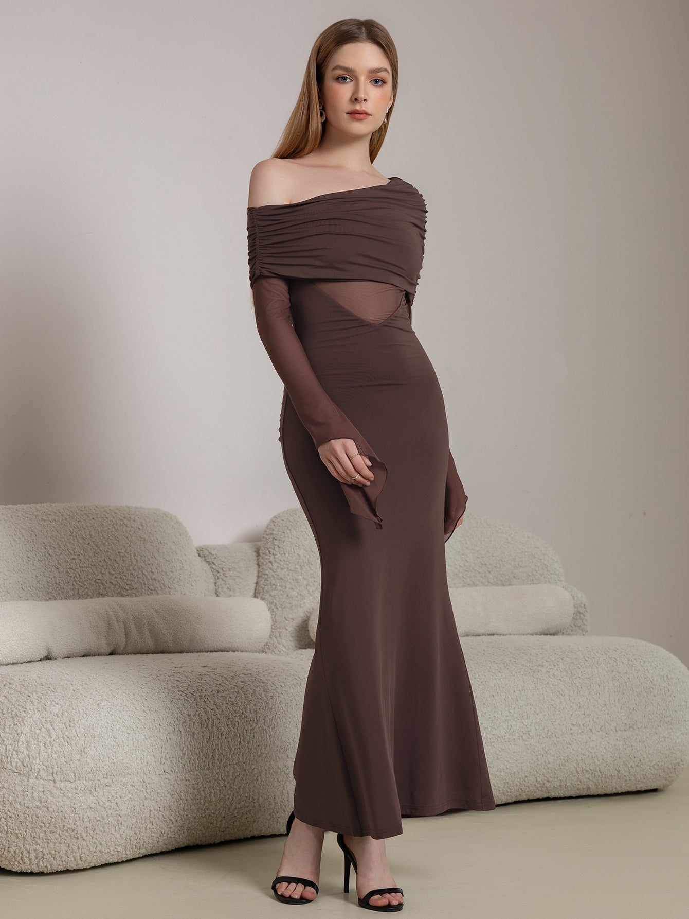 Model posing in a long brown ruched dress with sheer elements