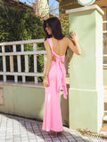 Back view of a woman in a pink one-shoulder maxi dress with an open back and tie detail.