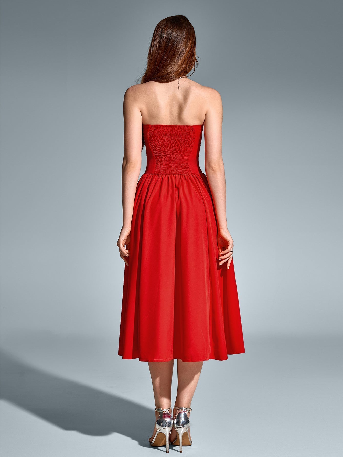 Back view of a woman in a red strapless satin midi dress with a sweetheart neckline and fitted waist.