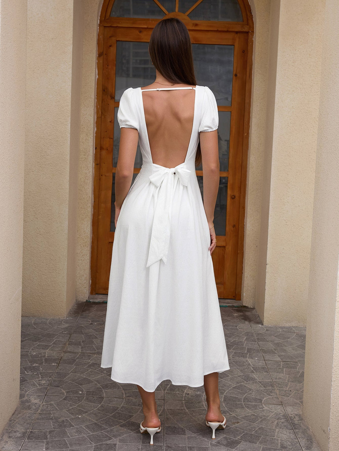 Woman wearing a white midi dress with puff sleeves and a scoop neckline, accessorized with a straw hat and a small handbag.