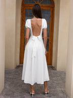 Back view of a woman in a white midi dress with an open back tied with a bow.