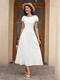 Woman wearing a white midi dress with puff sleeves and a scoop neckline, accessorized with a straw hat and a small handbag.
