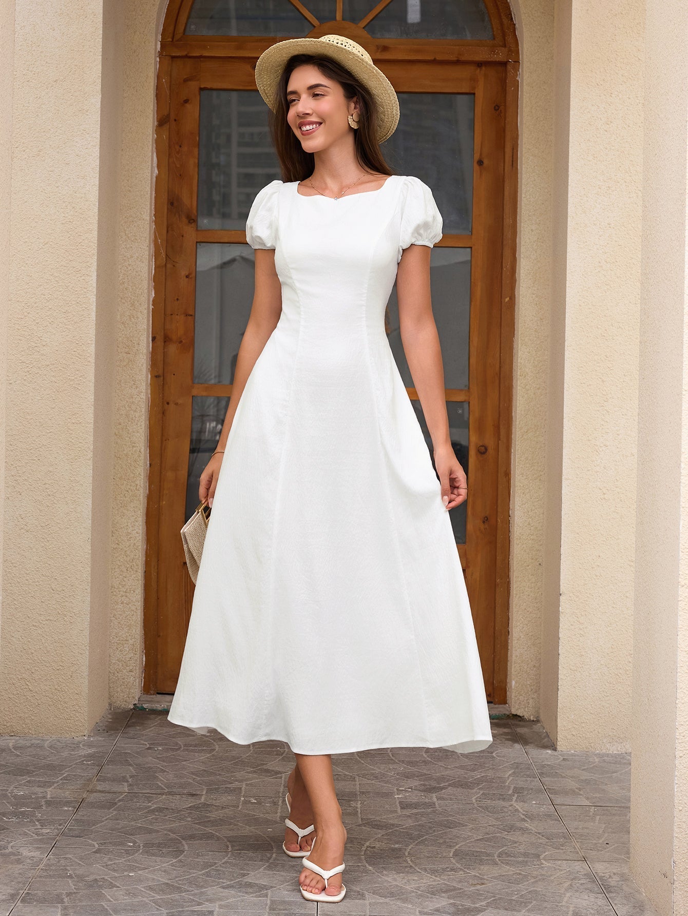 Woman wearing a white midi dress with puff sleeves and a scoop neckline, accessorized with a straw hat and a small handbag.