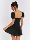 Back view of a woman in a black short puff sleeve square neck dress with a flared skirt.