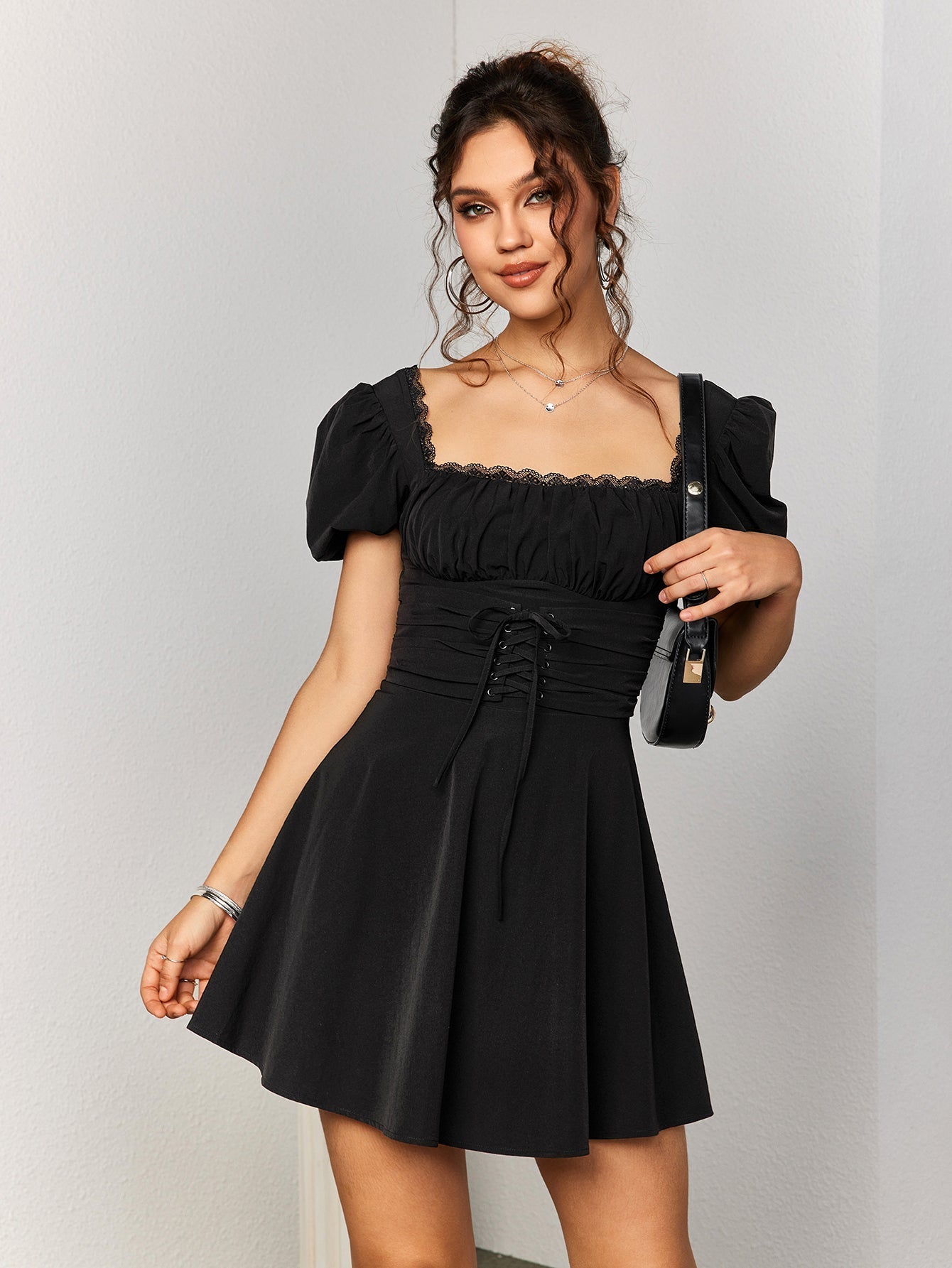 Woman holding a black handbag while wearing a black short puff sleeve square neck dress.