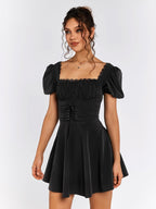 Front view of a woman in a black short puff sleeve square neck dress with a cinched waist.