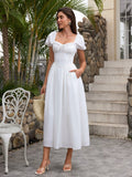 Woman holding a straw bag and wearing a white puff sleeve midi dress with a square neckline and corset bodice.