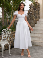 Woman in a white puff sleeve midi dress with a square neckline and corset bodice, standing next to a chair outdoors.