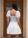 Back view of a woman in a white short dress with puff sleeves and a square neckline.