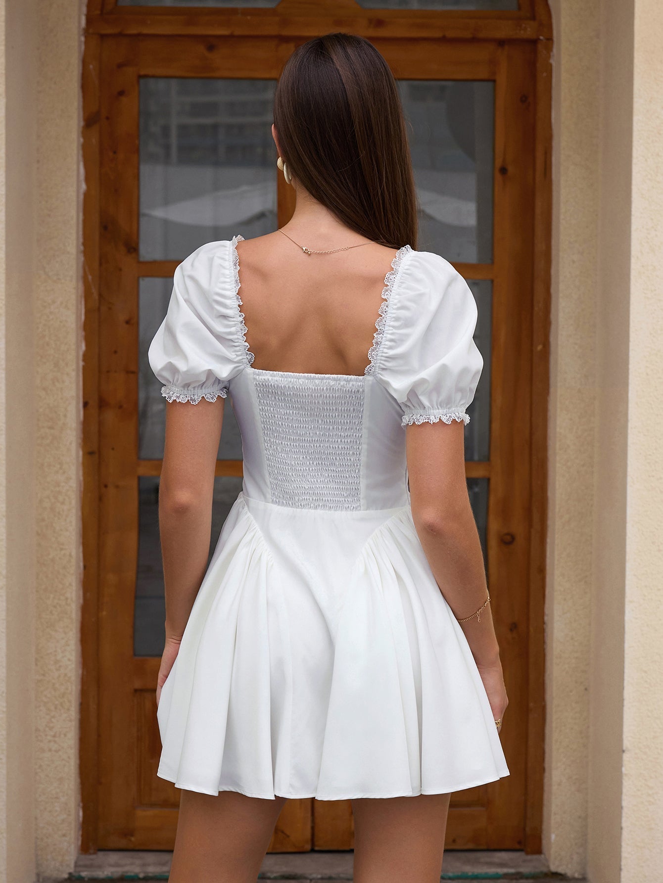 Back view of a woman in a white short dress with puff sleeves and a square neckline.