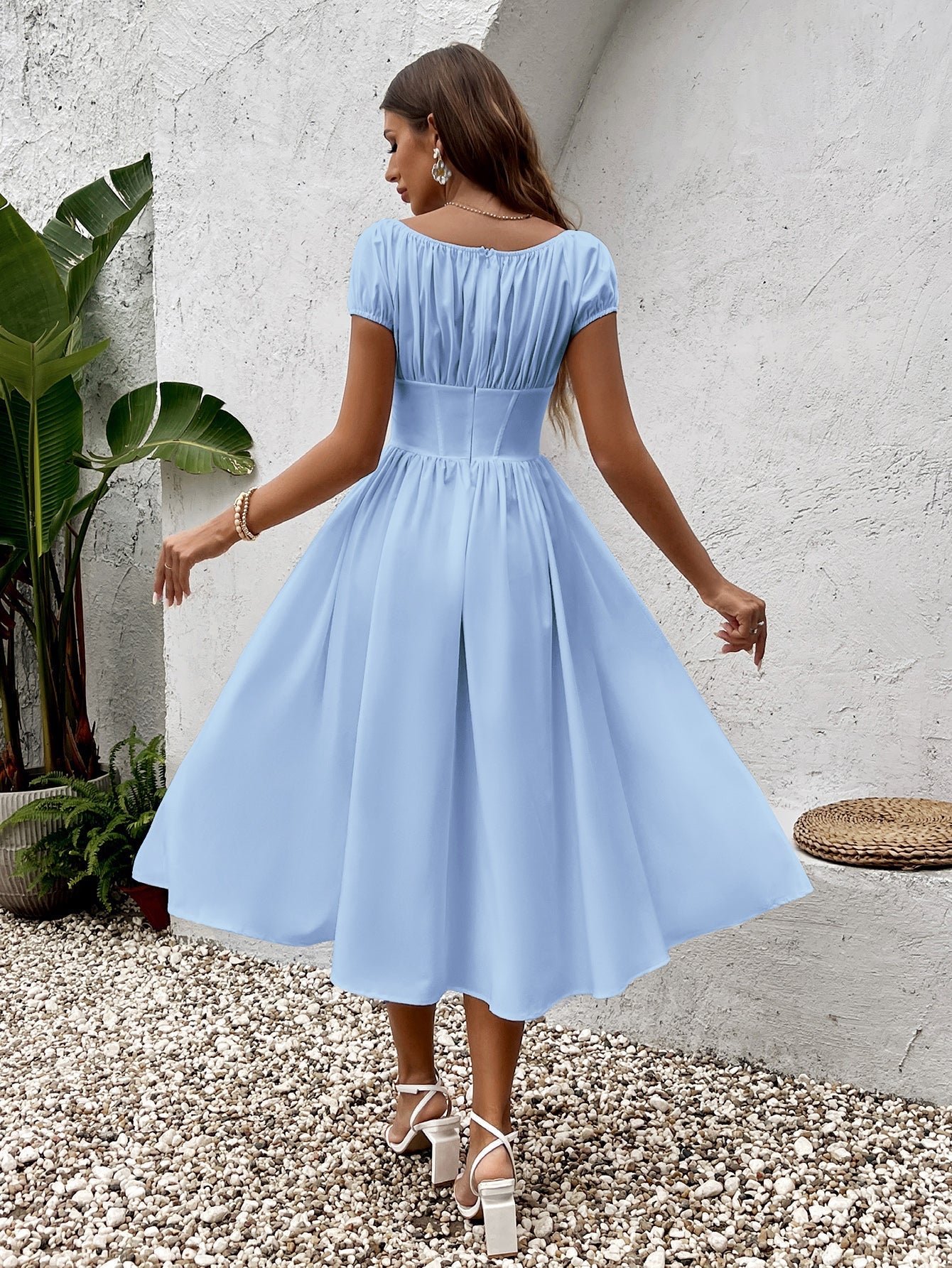 Back view of a woman in a light blue chiffon midi dress with a cinched waist and full skirt.