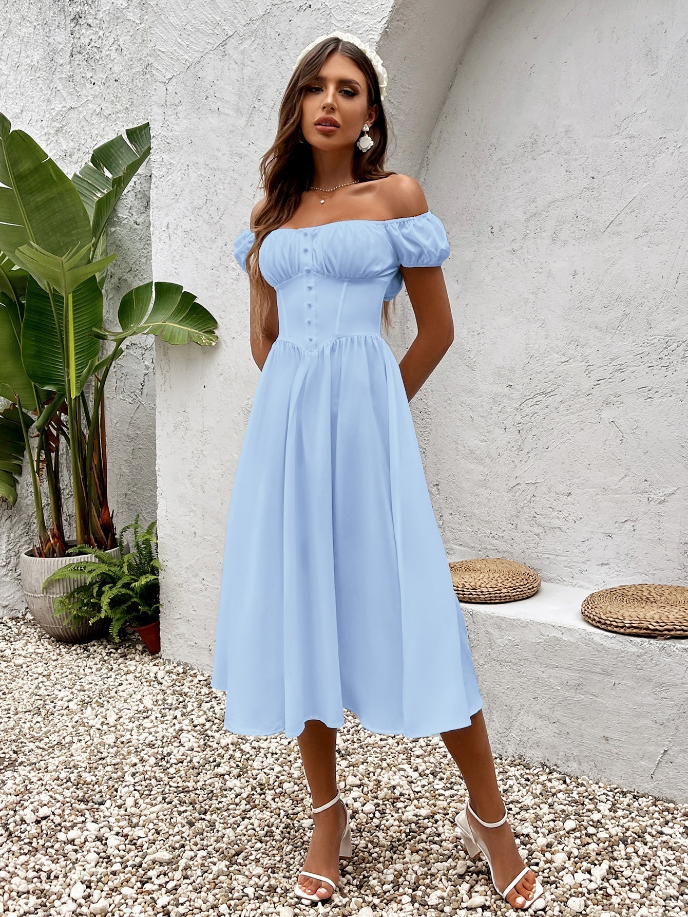 Woman in a light blue chiffon midi dress with a square neckline and cinched waist, standing outdoors.